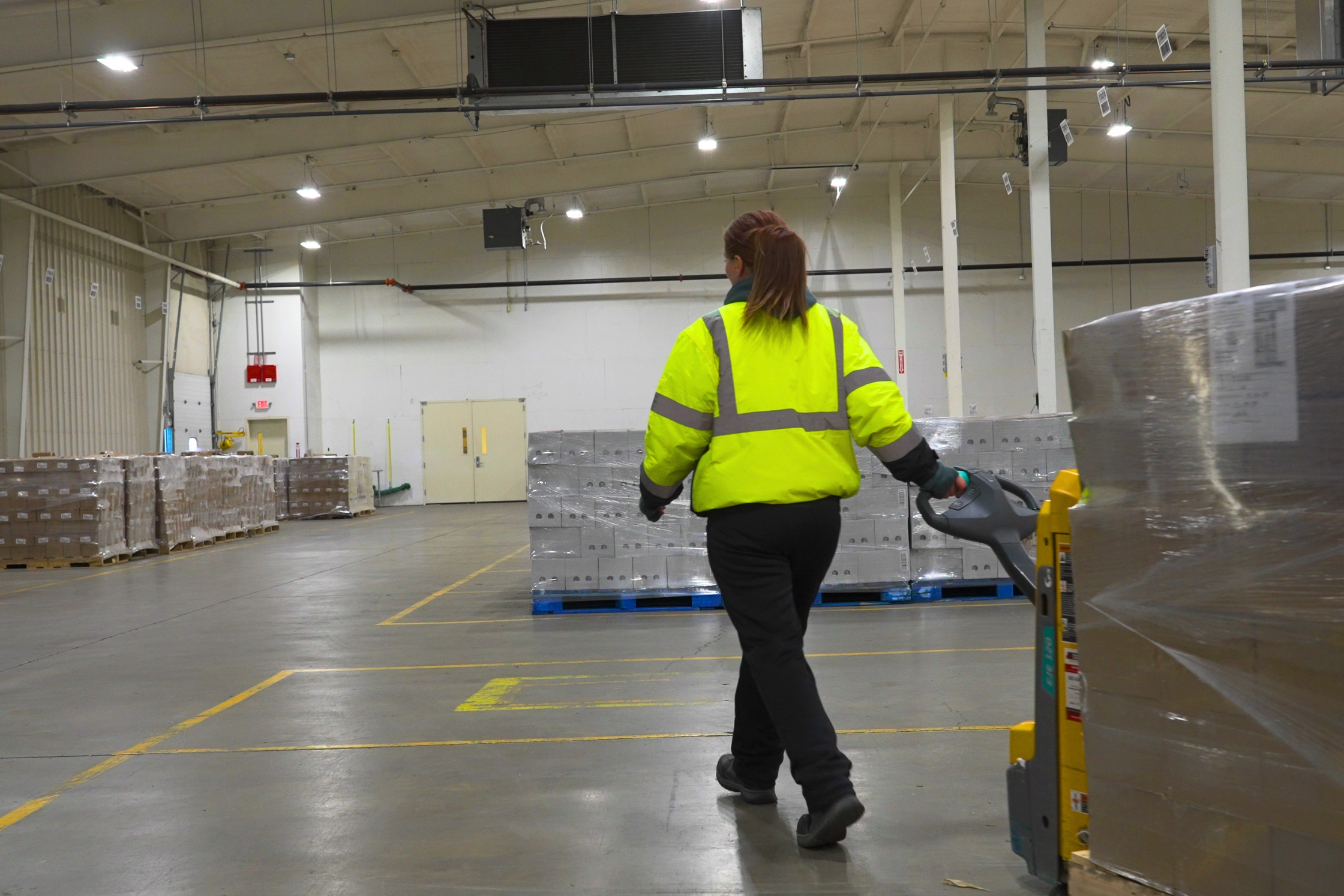 Contract Packaging teammate in HiVis dragging a pallet of product through temp-controlled warehouse.